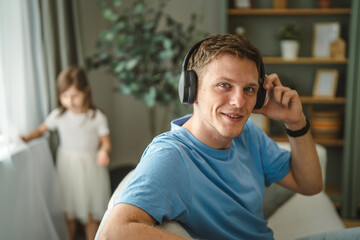 Fototapeta premium Father enjoying music with headphones while daughter playing at home