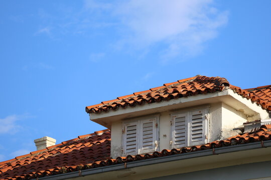 Traditional Mediterranean terracotta roof with dormer windows against blue sky