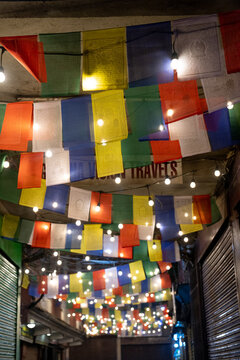 Kathmandu, Nepal - 04 April 2025: View of colorful prayer flags hanging across a narrow street in the Thamel district, illuminated by warm string lights at night.
