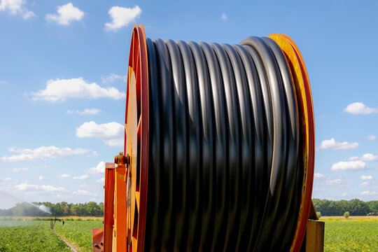 Sumer countryside landscape, Large industrial hose reel irrigator watering a crop field under blue sky with white cloud, Farming irrigation technology system spraying water, Agriculture in Netherlands