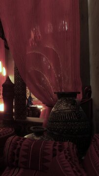 A room features colorful fabrics and pottery. The space shows a glimpse of cultural decor. Soft light filters through the fabric. The atmosphere hints at a cozy setting.