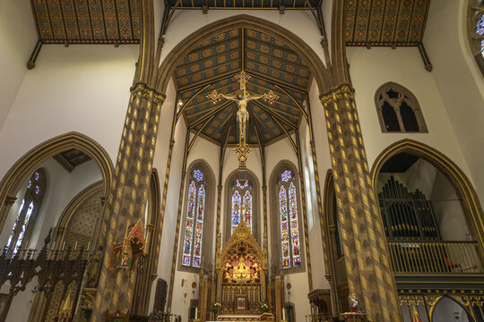 Birmingham, United Kingdom - 20 July 2026: View of the interior of St Chad's Cathedral, featuring a suspended crucifix above the altar, gothic columns, and vibrant stained glass.