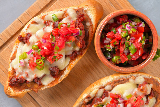 Mexican mollete with melted cheese, refried beans, chorizo and pico de gallo topping, overhead view