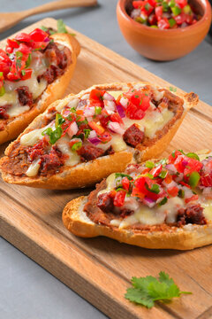 Traditional Mexican open faced sandwich mollete served on a wooden board with cilantro garnish