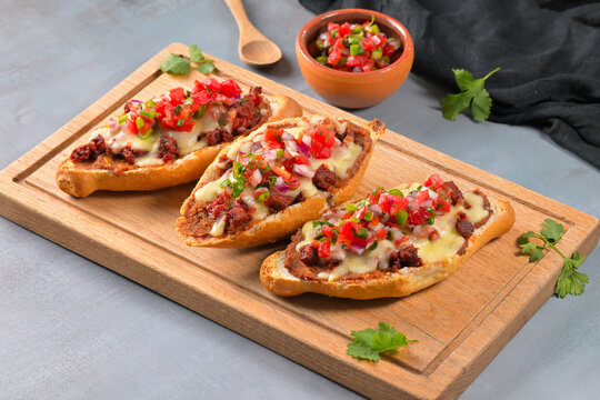 Traditional Mexican molletes with refried beans, melted cheese, chorizo and fresh pico de gallo salsa on a wooden board