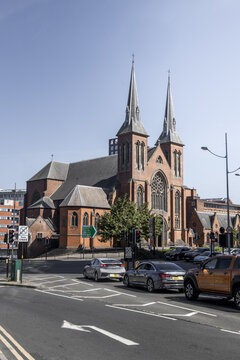 Birmingham, United Kingdom - 20 July 2026: View of St Chad's Cathedral with its distinctive twin spires and red brick facade, seen from a busy street corner under a clear blue sky.