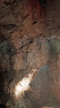 A light source highlights a rock formation inside a cave. The cave has rough stone walls, and some greenery appears near the ground. The scene shows natural textures and shapes.