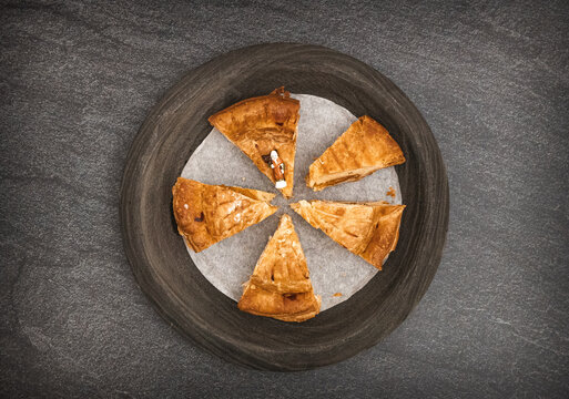 Five cut pieces of galette de rois, a figurine and a crown in a plate.