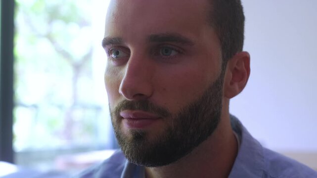 Close-up portrait of a thoughtful young man with a beard and blue eyes meditating and then opening his eyes, looking away with a serene and calm expression in a peaceful environment