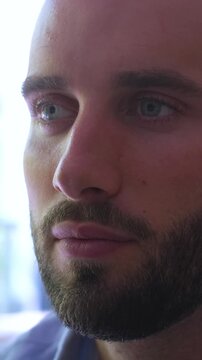 Close-up of a handsome young bearded man meditating with his eyes closed, then slowly opening them to look forward with a serene and thoughtful expression in a bright, sunlit room