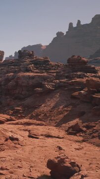 Dusty ground and rock formations are visible under the bright sun. The scene shows a rugged area with steep hills in the background.
