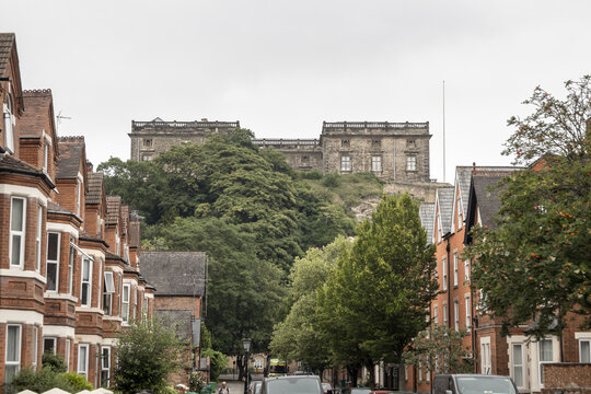Nottingham, United Kingdom - 15 July 2026: View of Nottingham Castle rising above traditional red brick terraced houses and lush green trees under an overcast sky.
