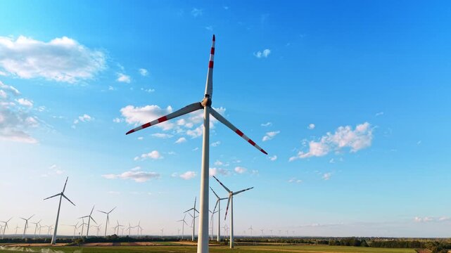 Large wind turbine towering into a clear blue sky. A low angle shot shows the steel tower and red striped blades of a modern wind generator over a distant horizon.