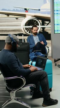 Vertical video: African American casual man uses AI neural networks in an airport lounge, applying deep learning and analytics to business development during an international work trip with a laptop.