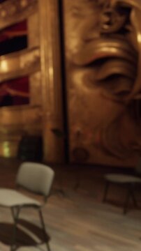 Chairs are arranged in front of a large decorative wall inside a theater. The space has a rich history and is set up for an event or gathering. Light reflects off the gold elements.