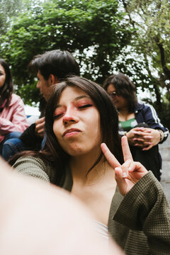 Close up portrait of a young Hispanic woman making a peace sign and a funny face for a smartphone selfie