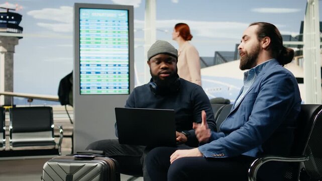 Two male consultants type on a laptop in an airport waiting area, analyzing data and preparing for an international business meeting and global work delegation before their overseas flight.