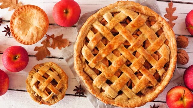 Homemade autumn apple pies, overhead view table scene with a white wood background. Slow rotating zoom motion.