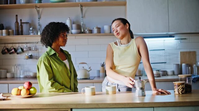 Multiethnic girlfriends brewing coffee moka pot kitchen. Two women chatting.