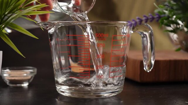 Water is being poured from a glass carafe into a measuring cup in the kitchen (close-up).