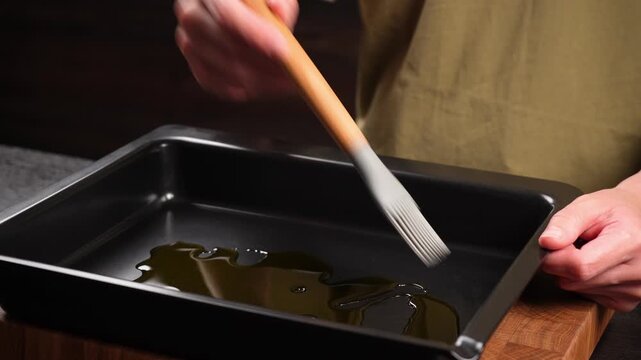 The chef greases the baking sheet with olive oil using a silicone pastry brush.