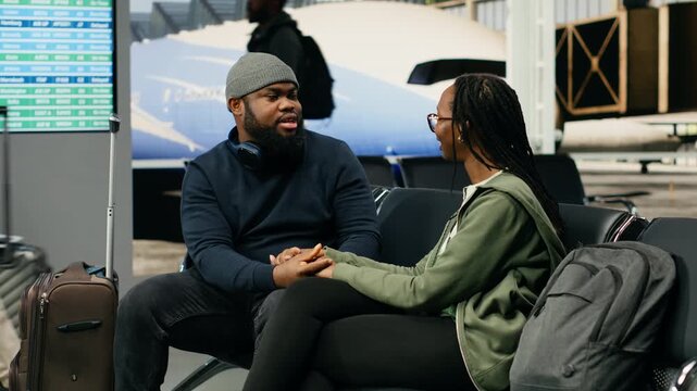 African American lovers laugh together in an airport terminal, holding hands while planning sightseeing attractions and a romantic vacation trip before departure during holiday travel.