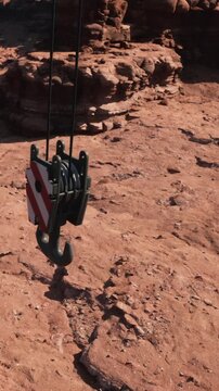 A heavy equipment hook is suspended from a pulley system. It is positioned over rocky terrain with uneven surfaces, indicating an industrial or construction activity.