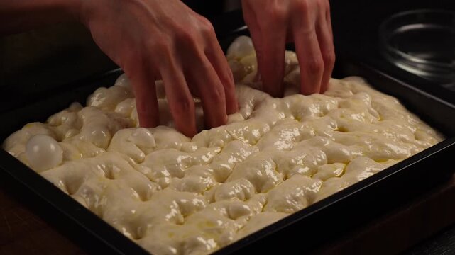 Fingers sink into the soft, airy focaccia dough, brushed with olive oil, on the baking sheet.