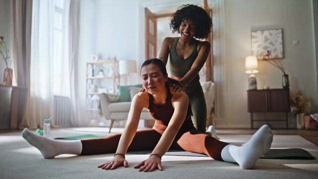 Fitness coach helping woman deep stretch splits home. Yoga training living room.