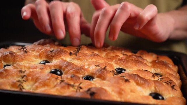 Fingers tapping on the delicate, golden, crisp crust of a fresh, hot olive focaccia close up.