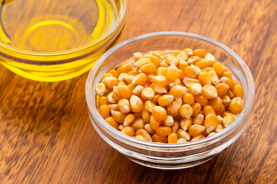 Popcorn kernels and vegetable oil resting in glass bowls on a wooden background