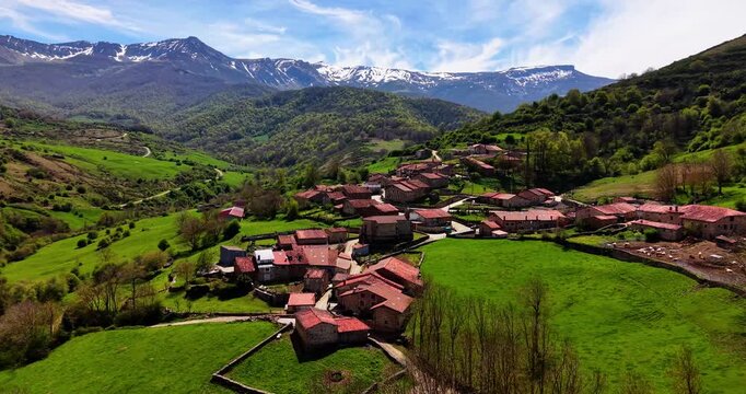 Idyllic mountain hamlet with traditional stone houses nestled in a green valley under snow capped peaks