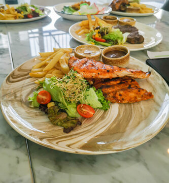 Grilled salmon served with french fries and fresh salad on ceramic plate in restaurant setting. Balanced healthy meal with protein, vegetables, and modern dining presentation.