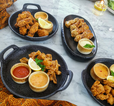 Crispy fried chicken served with assorted dipping sauces and lemon wedges on black plates. Top view appetizer platter concept for sharing meal in modern restaurant setting.
