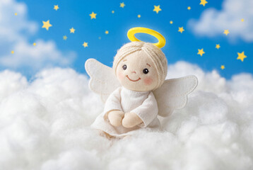 Obraz premium Cute fabric angel doll with a yellow halo sits on fluffy white clouds beneath a starry blue sky