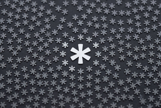 Large white asterisk symbol standing out among many small dark grey asterisks on a flat background
