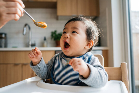 Asian baby boy in high chair waiting to be fed with spoon