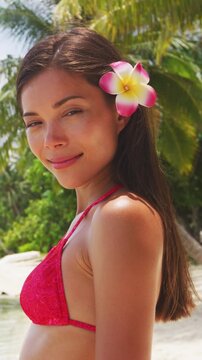 Beach beauty woman Natural exotic babe in red swimsuit looking serene on tropical beach. Asian bikini model wearing hibiscus flower for body care pampering. Vertical video of real woman without makeup