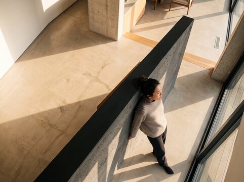 High angle view of a young woman leaning against a wall in a modern minimalist house illuminated by warm sunlight