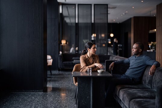 Diverse man and woman having a conversation in a modern luxury hotel lobby lounge during a business meeting