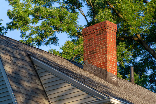 Red brick chimney on a sloped house roof with asphalt shingles
