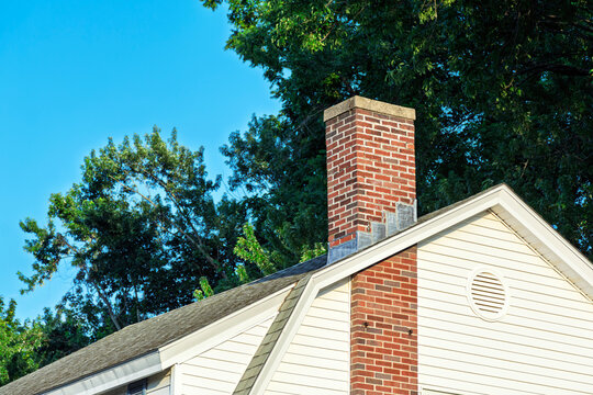 Red brick chimney on a sloped house roof with horizontal white siding