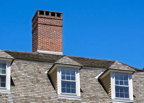 Red brick chimney and dormer windows on a gambrel roof with wood shingles
