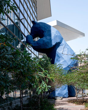 Denver convention center, with a giant blue bear standing and peering through glass winder under a sunny summer day