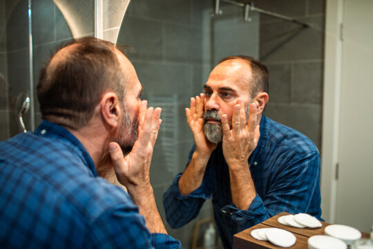 Middle-aged man applying moisturizer in home bathroom mirror