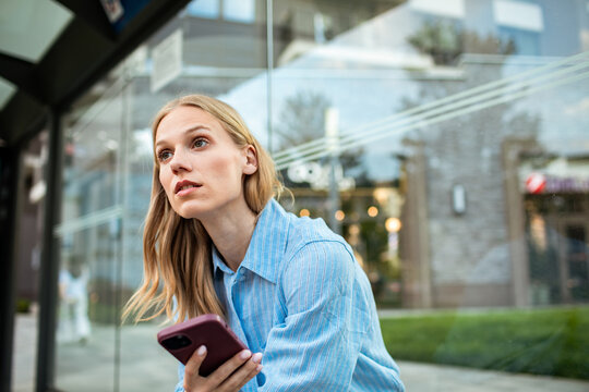 Young woman waiting with smartphone at city bus stop