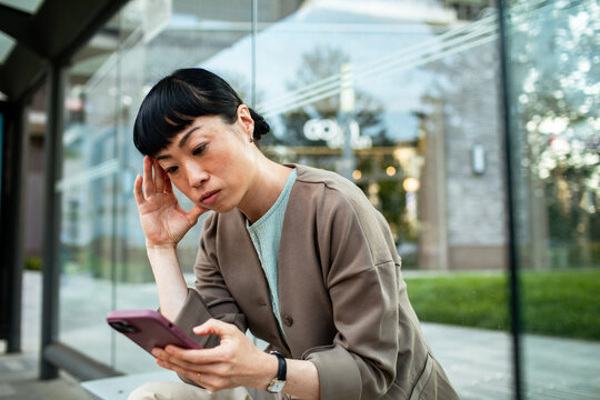 Concerned woman checking smartphone at bus stop