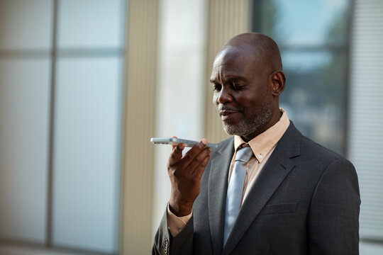 Mature businessman using smartphone voice assistant outside office building