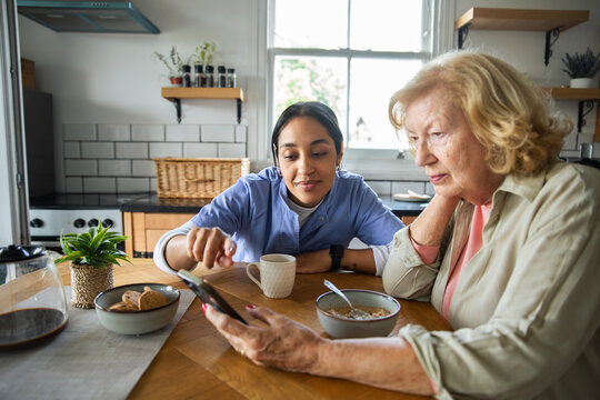 Caregiver helping senior use smartphone at home kitchen table