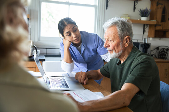 Home caregiver helping senior man with laptop at kitchen table